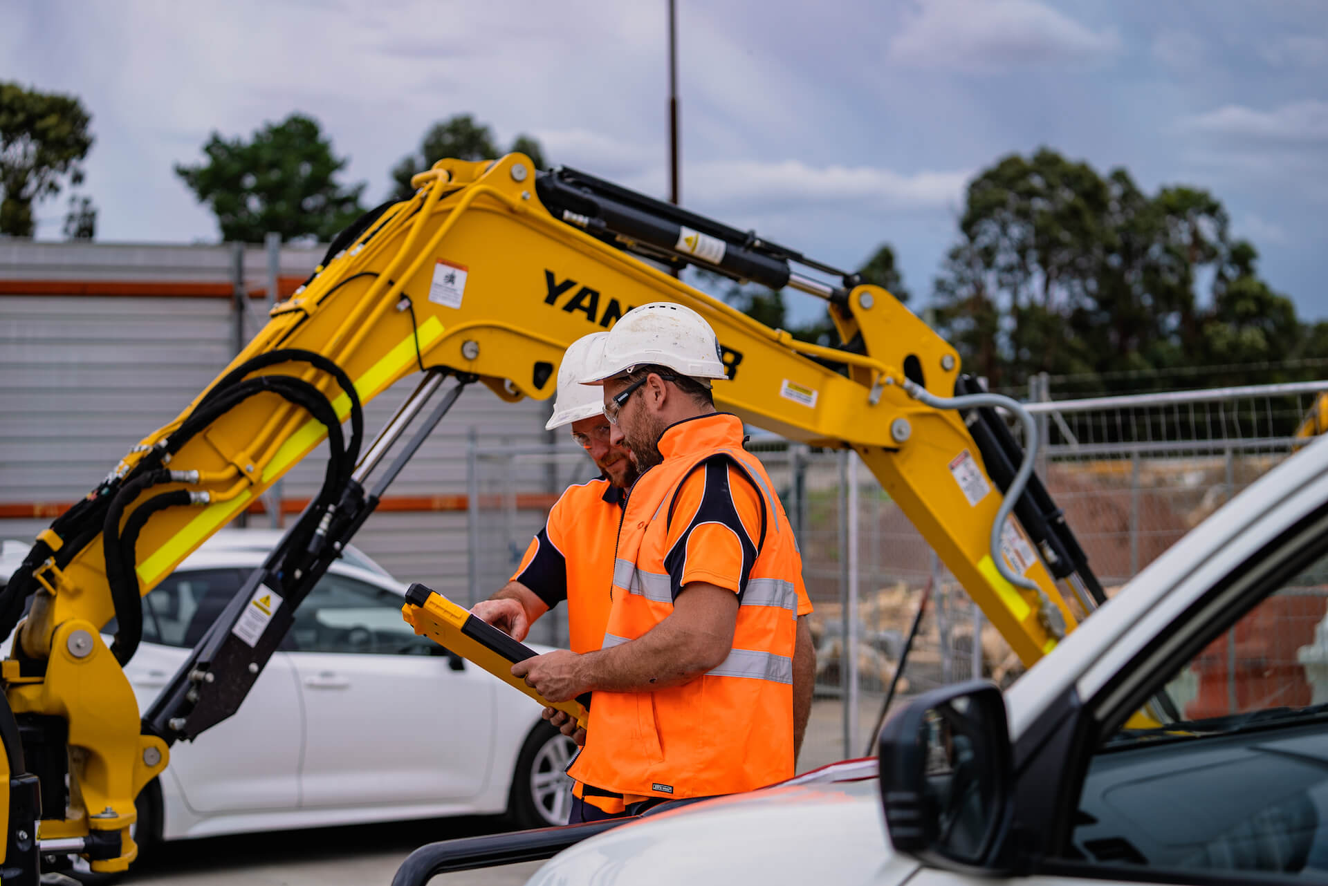 Two plumbers inspect the groudns at Fire Service VIC as a bulldozer is parked behind them.